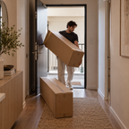 A man carrying one of the two cartons through an apartment front door, the other carton already inside the hallway