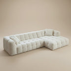 A woman sits down on the Cloud Corner Sectional in Cloud White and the bouclé cushions compress beneath her